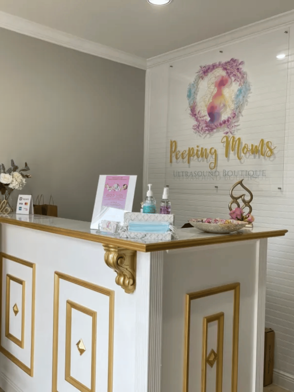 Gold & White front desk with Peeping Moms Ultrasound logo in background
